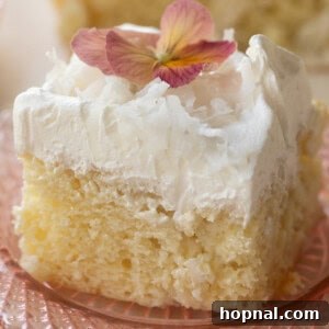 Fluffy slice of coconut poke cake with whipped frosting and shredded coconut.