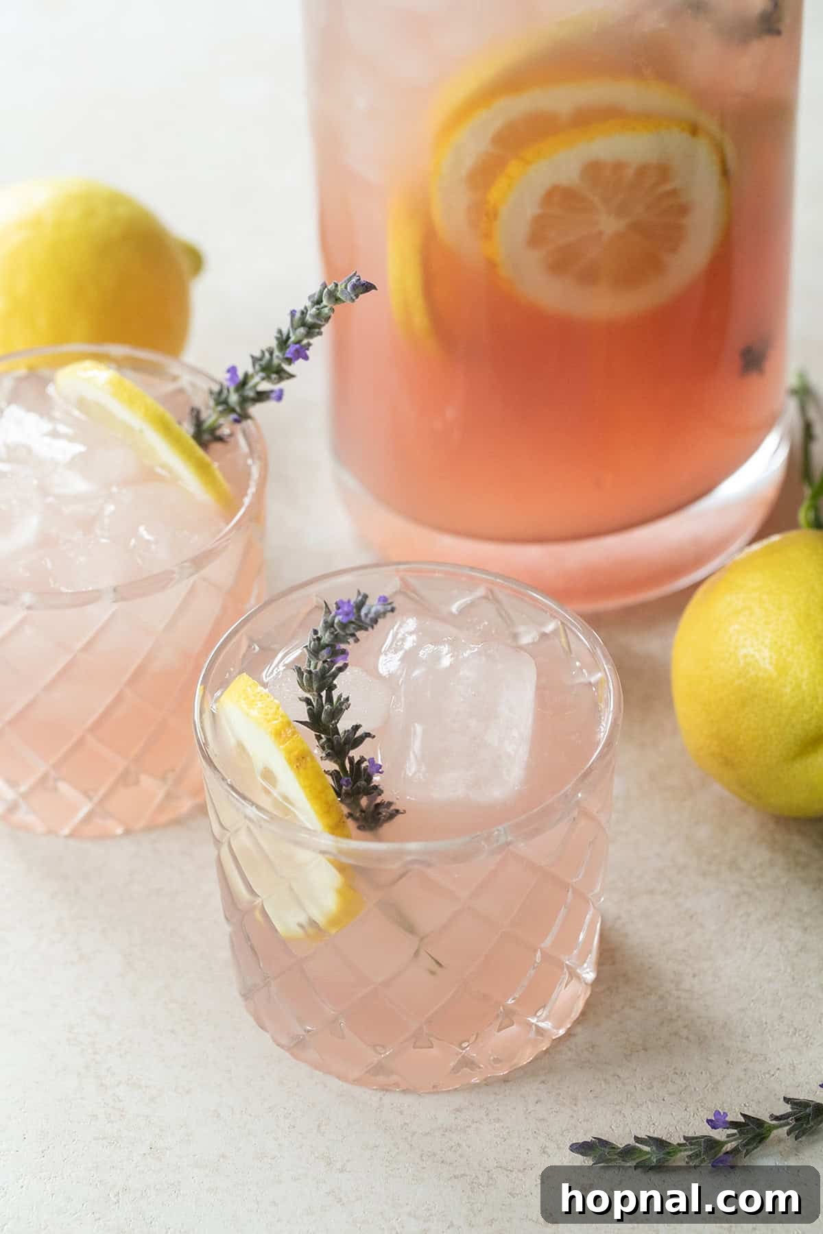 Two glasses of lavender lemonade garnished with lemon slices and fresh lavender sprigs, surrounded by fresh lemons and lavender blooms.