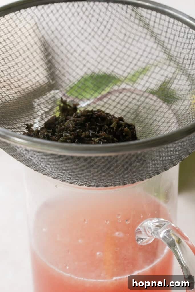 Straining dried lavender from the syrup into a pitcher already containing fresh lemon juice, ensuring a smooth lemonade.