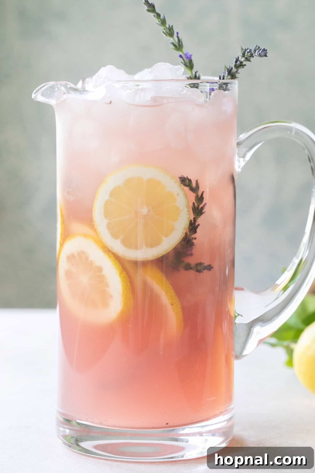 A pitcher of homemade lavender lemonade with fresh lemon slices and lavender sprigs, surrounded by flowers, evoking a refreshing summer scene.