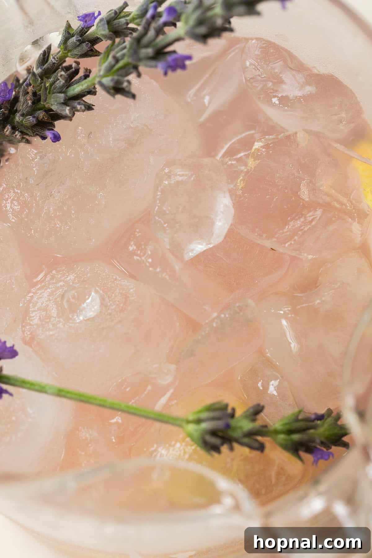 A refreshing glass of lavender lemonade with ice and a lemon slice, placed on a rustic table outdoors.