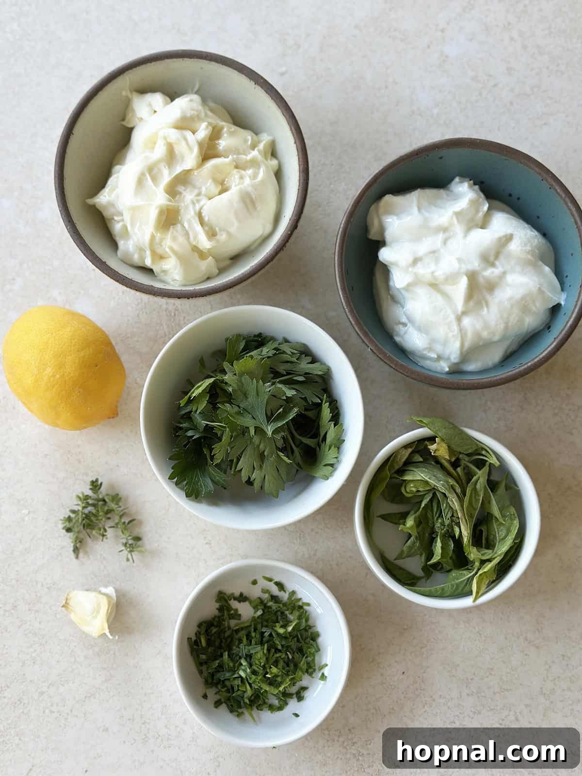 Bowls filled with fresh herbs, Greek yogurt, mayonnaise, garlic, and citrus halves, ready to be combined for green goddess dip.