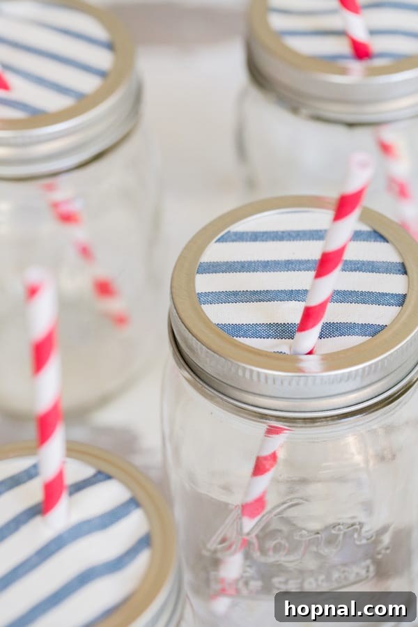 Party Perfect Festive Jar Decor 7 A charming display of various Ball canning jars, each topped with a different patterned fabric lid, featuring straws for a delightful party drink setup.