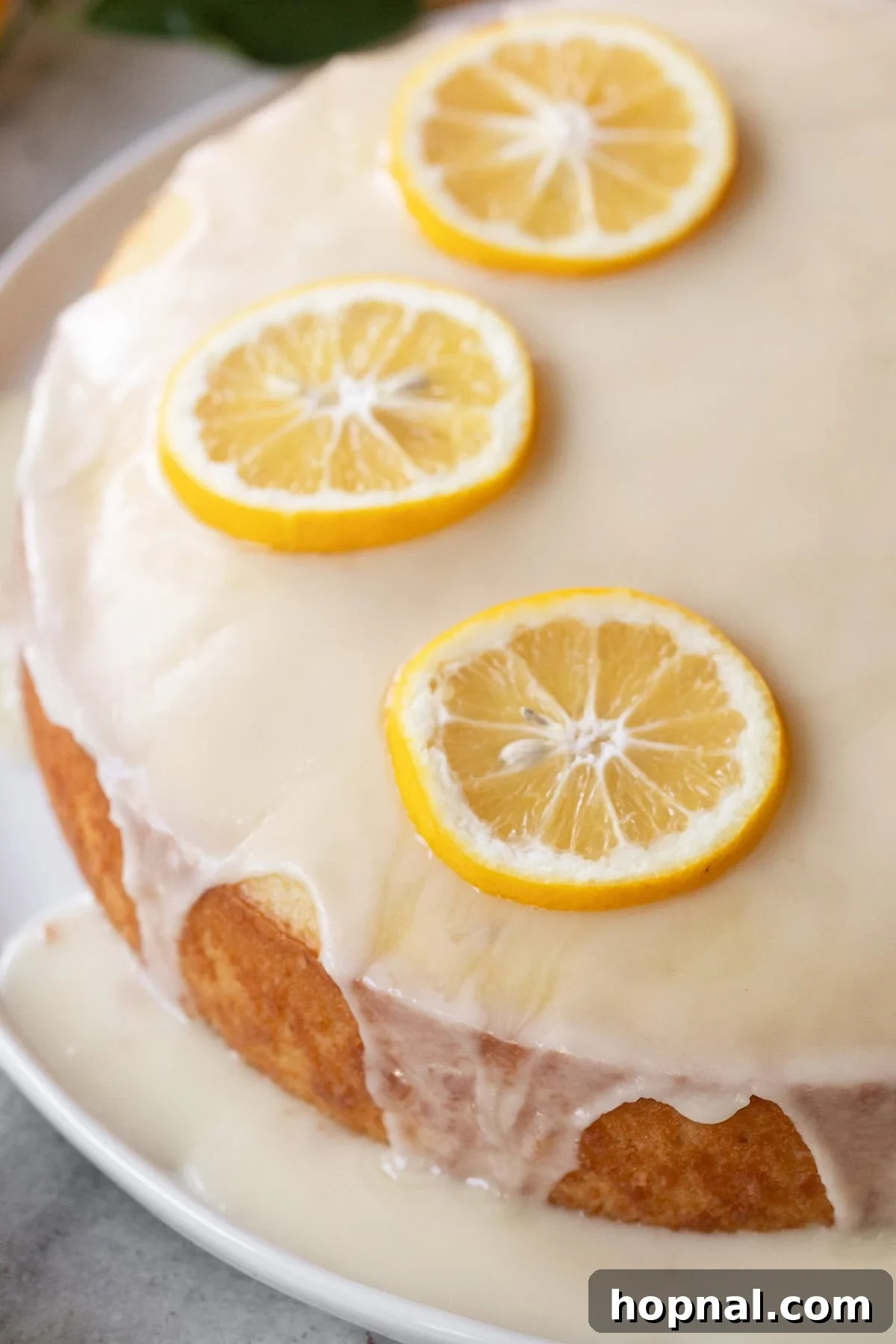 Close-up of moist lemon olive oil cake with lemon glaze and fresh lemons.