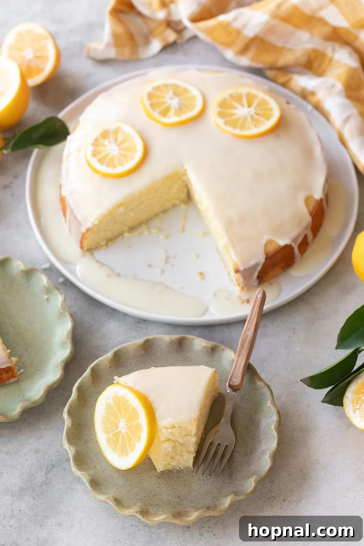 Lemon olive oil cake on table with slice removed green plates yellow napkins and fresh lemons.