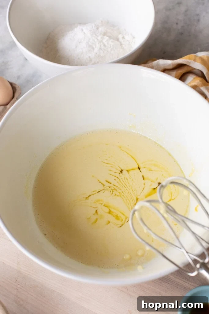 Olive oil drizzled into lemon olive oil cake batter in mixing bowl.