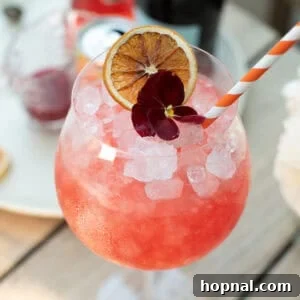 Blood orange spritz in a large wine glass with crushed ice and a blood orange slice garnish.