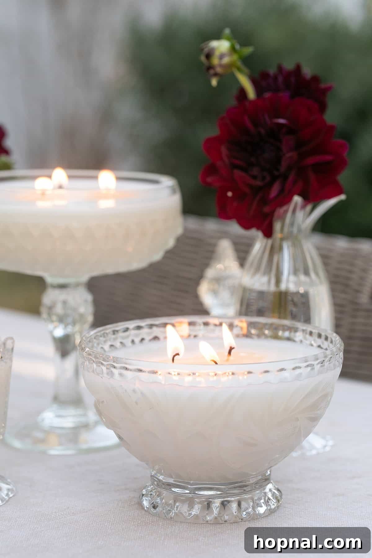 Homemade candle poured in a vintage glass vessel, lit on a table with flowers.